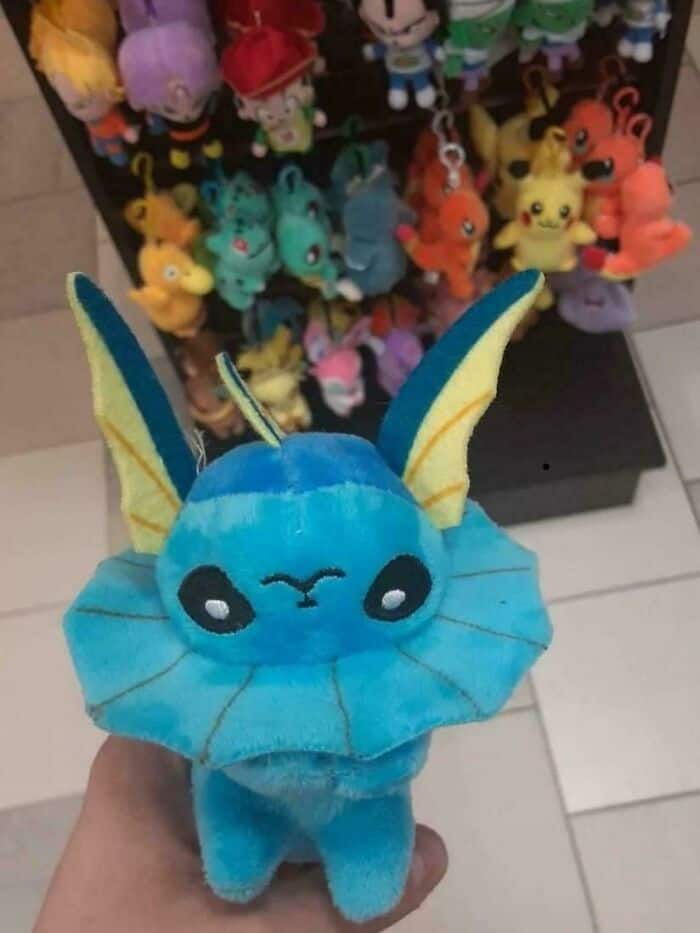 bootleg toy funny fail featuring a Vaporeon plushie. The manufacturer accidentally sewed the creature's neck ruff directly onto its face, resulting in a deformed, wide-eyed Pokemon that looks more like a frilled lizard than a water-type.