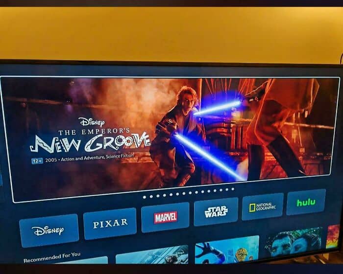 A streaming service funny fail where a TV screen displays the title and logo for Disney’s The Emperor's New Groove, but the background image is actually the high-stakes, fiery lightsaber duel between Anakin and Obi-Wan from Star Wars: Revenge of the Sith.
