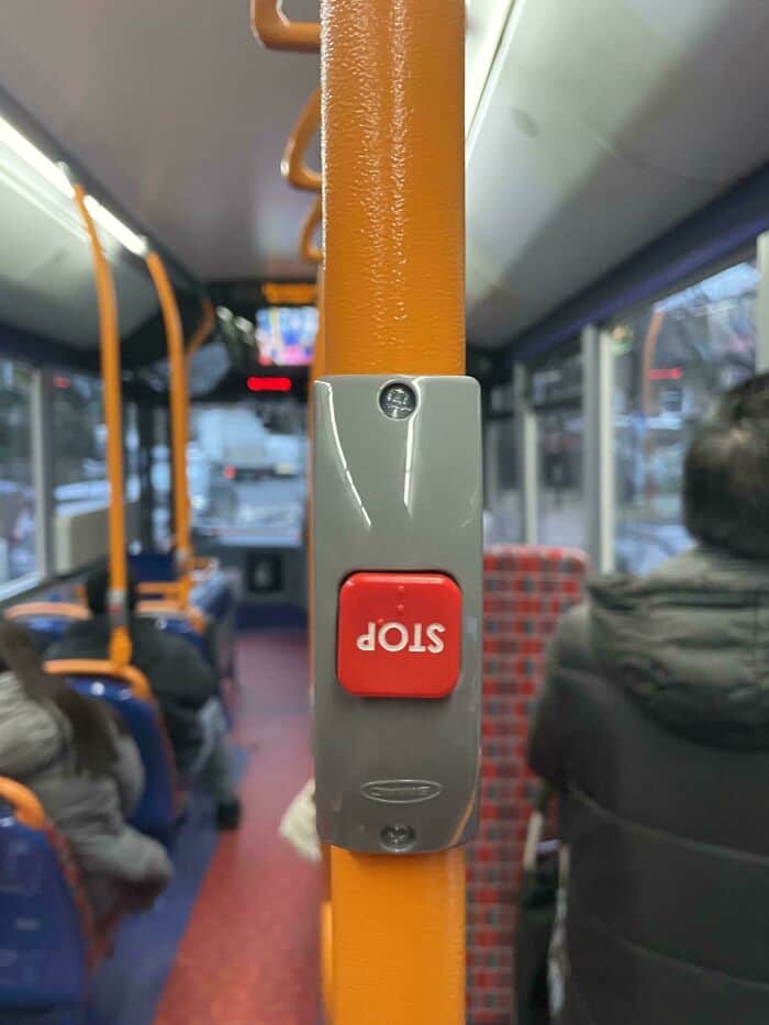 A low-effort installation funny fail on a public bus. The red "STOP" button has been mounted completely upside down, making the text orientation a minor but annoying visual grievance for passengers.