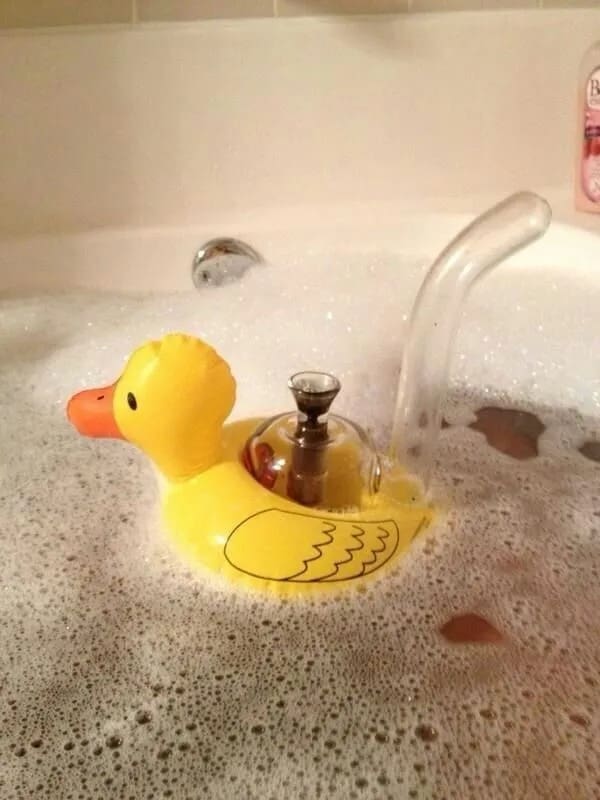 Funny image of a glass bong shaped like a rubber ducky floating in a bubble bath.