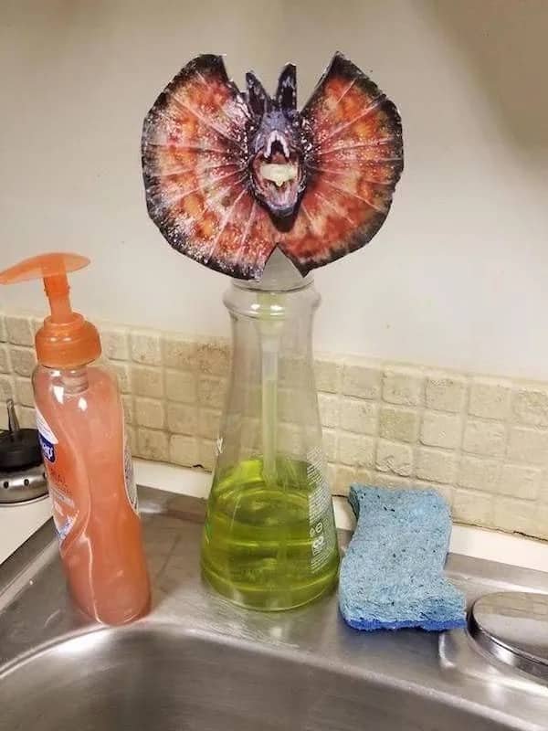 A dish soap dispenser decorated with a paper cutout of a Dilophosaurus from Jurassic Park.