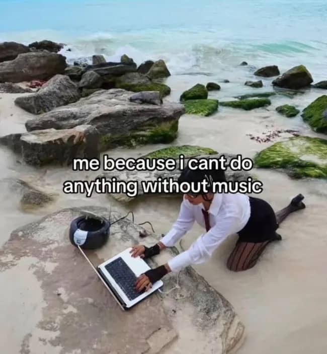 Funny image of a woman using a laptop and portable CD player on a beach.