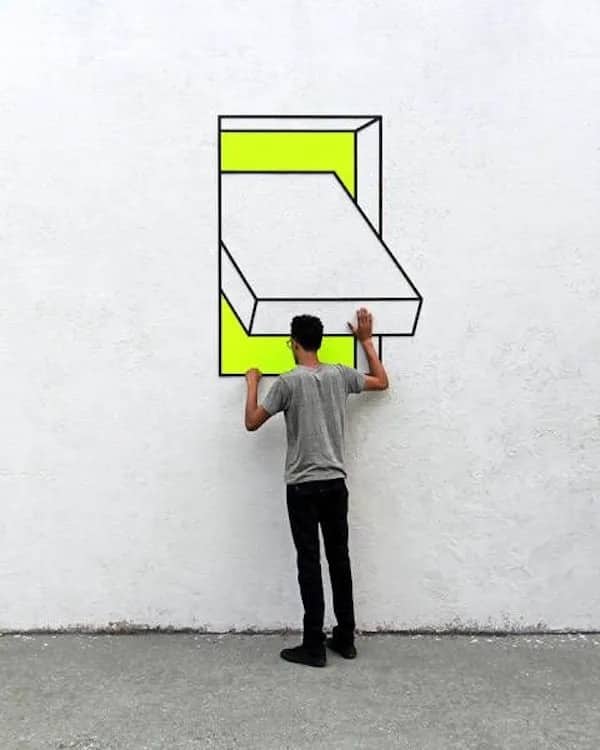 Street art featuring a man appearing to pull a 3D rectangular block out of a wall.