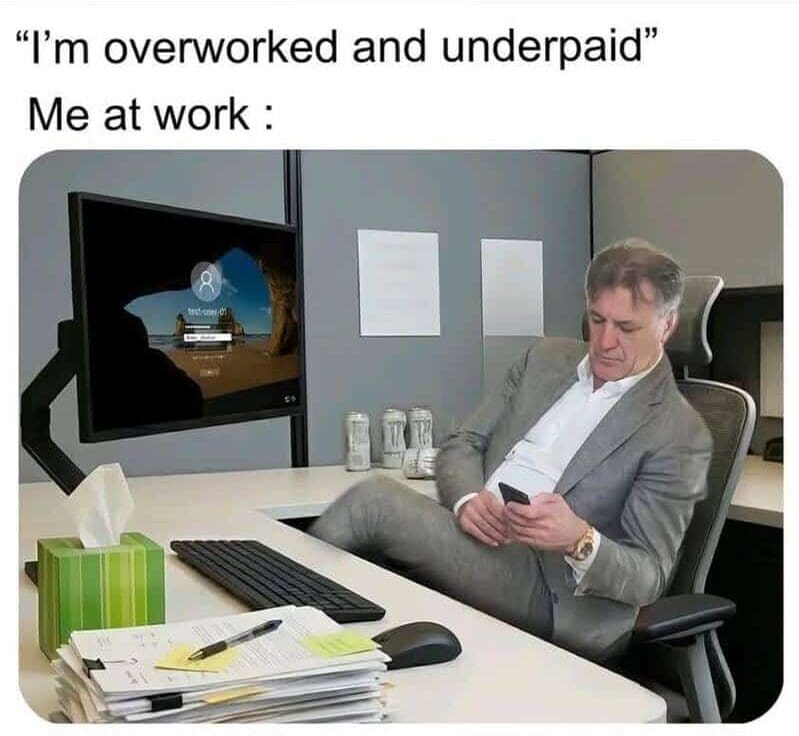 A hilarious work meme exposing the irony of claiming to be overworked and underpaid while showing an employee kicking their feet up on a desk to strictly scroll on their phone in front of a locked computer screen.