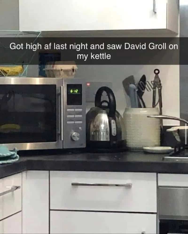 Stainless steel kitchen kettle with a handle reflection that humorously resembles Dave Grohl’s facial features.