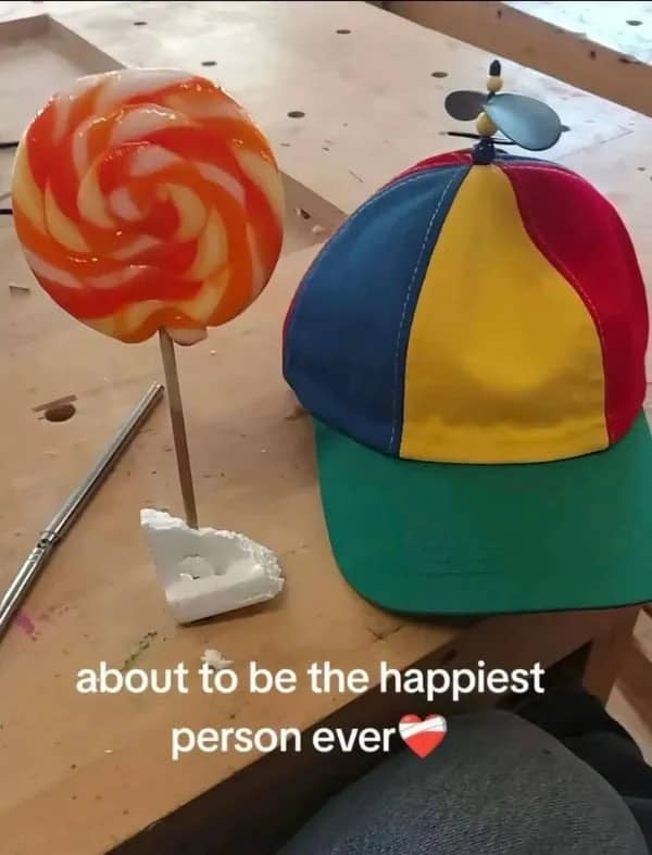 Large orange swirl lollipop next to a colorful propeller hat with a caption about being happy.