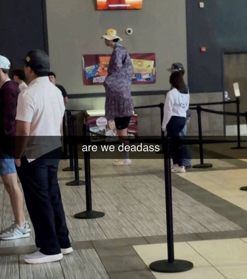 A funny photo of a very tall person in a long coat standing in line.