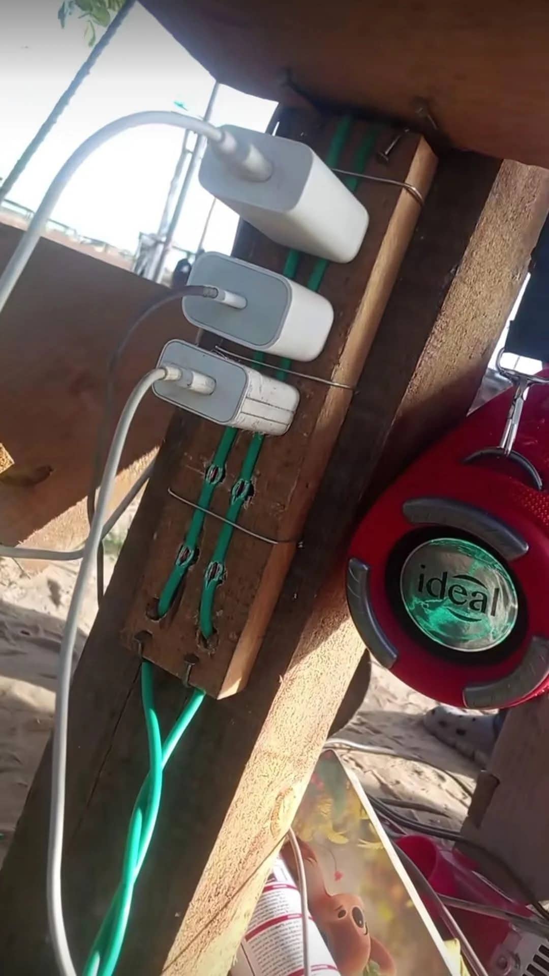 Homemade DIY power strip made from wood and wires charging multiple phone adapters outdoors.