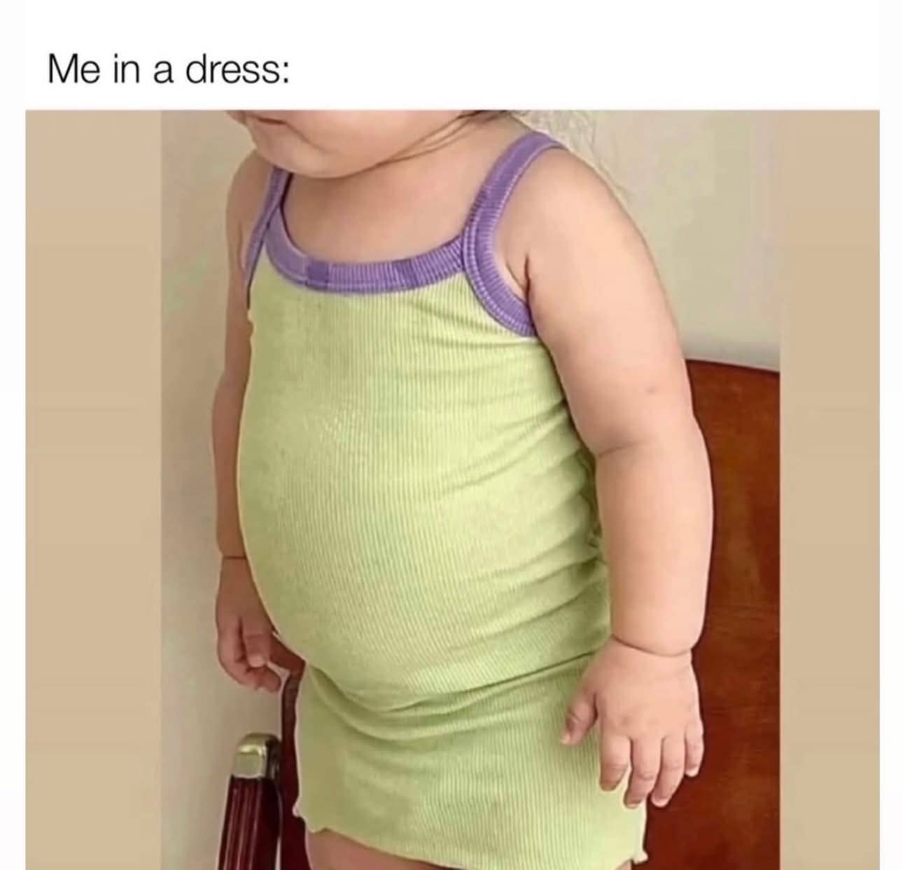 A young child wearing a tight green and purple dress, highlighting a rounded belly.