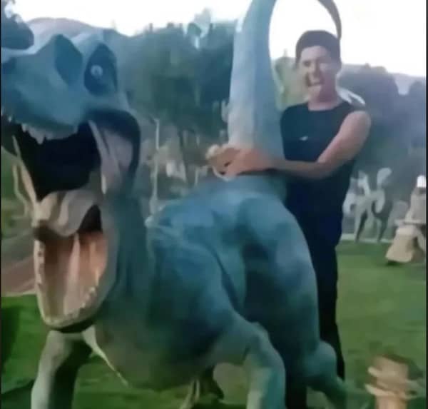 A blurry, chaotic image of a person interacting with a large blue dinosaur statue in a park.