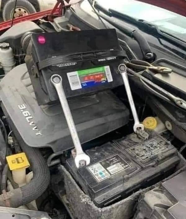 Car engine featuring a second battery connected to the first using two metal wrenches as jumpers.