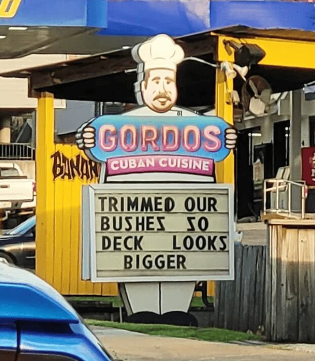 A cheeky funny sign outside a restaurant called Gordos Cuban Cuisine. The marquee under the chef mascot displays a classic bit of "lawn maintenance" double-entendre: "TRIMMED OUR BUSHES SO DECK LOOKS BIGGER."