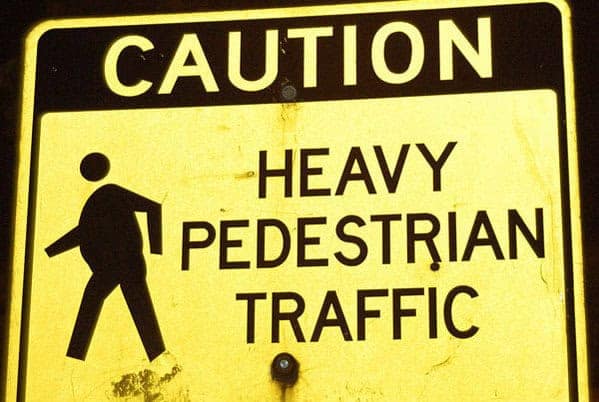 A literal-minded funny sign for "HEAVY PEDESTRIAN TRAFFIC." Instead of warning of high numbers, the yellow "Caution" sign features a silhouette of a person with a massive, round belly, implying the pedestrians themselves are physically "heavy."