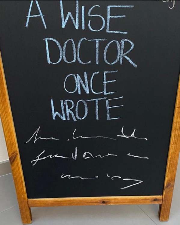 clever funny sign on a wooden-framed chalkboard. The top half reads, "A WISE DOCTOR ONCE WROTE," while the bottom half is filled with three lines of completely illegible, jagged scribbles, perfectly mimicking a physician’s infamous handwriting.