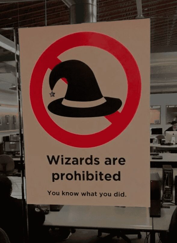 passive-aggressive funny sign found in an office setting. Below a large red "prohibited" circle over a black wizard hat, the text firmly states: "Wizards are prohibited. You know what you did."
