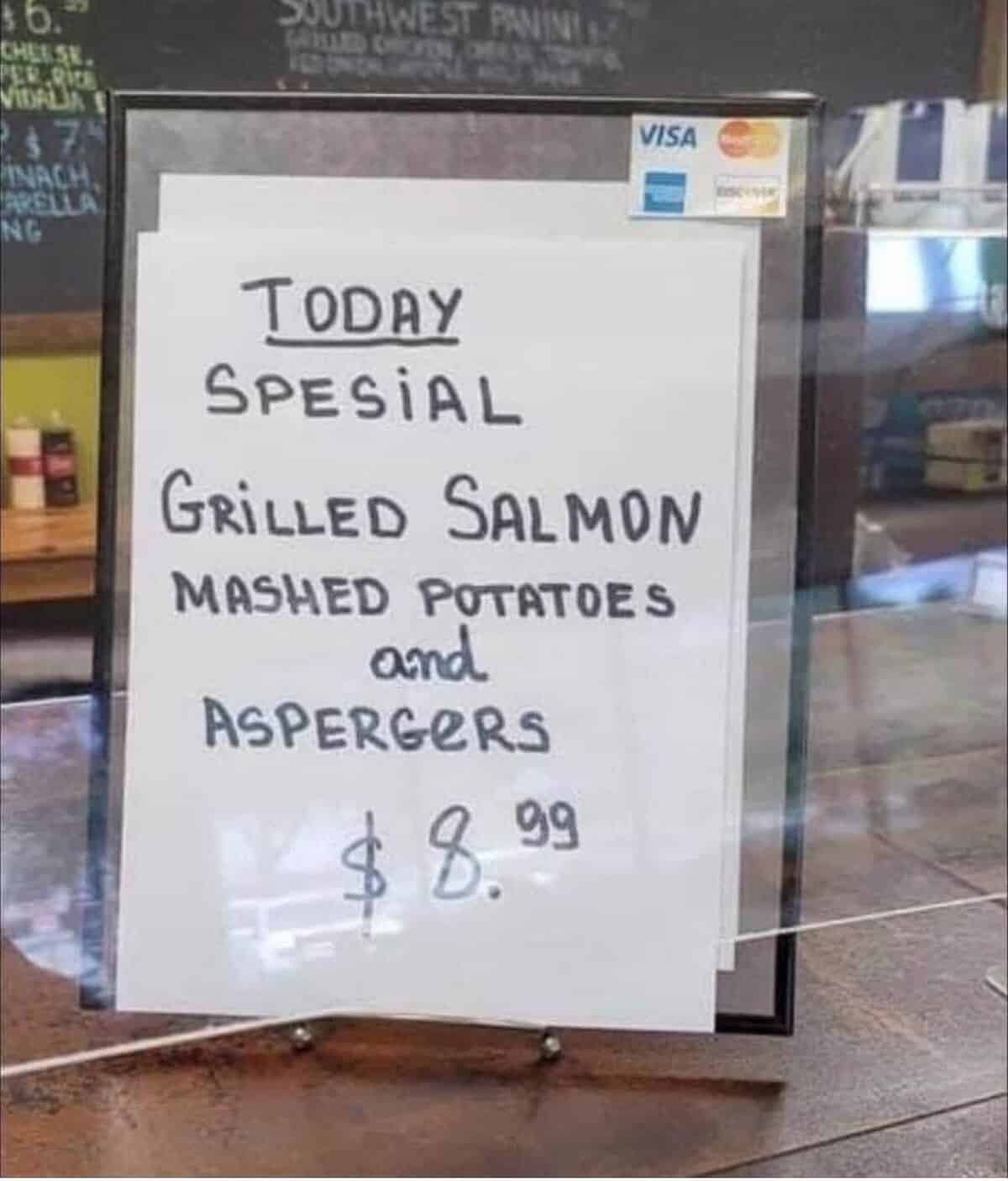 handwritten restaurant chalkboard sign offering a "spesial" of grilled salmon and "ASPERGERS," a truly unfortunate and funny spelling fail that meant to list "asparagus" as the side dish.