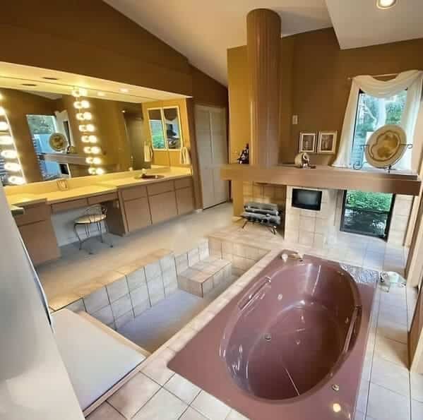 A carpeted bathroom featuring a large sunken bathtub and a fireplace built directly into the vanity.