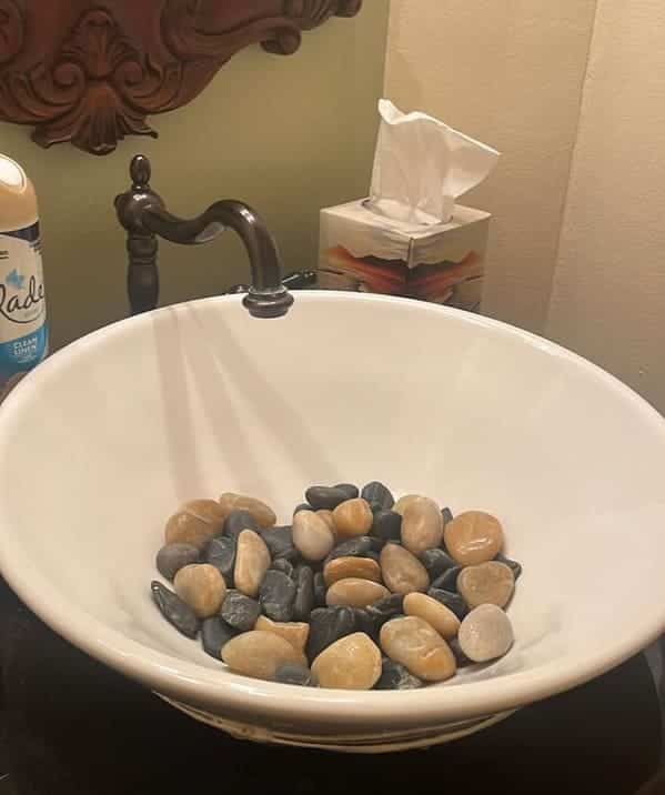 A white porcelain bathroom sink bowl filled with several dozen smooth decorative river stones.