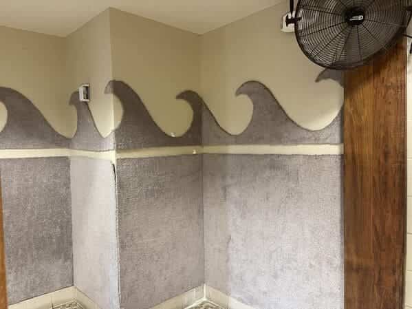 An interior room with wave-shaped wall molding covered in textured, grey carpet-like material.