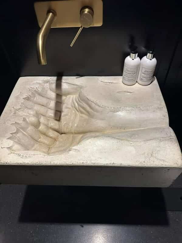 A concrete bathroom sink shaped like a pair of cupped human hands with deep crevices.