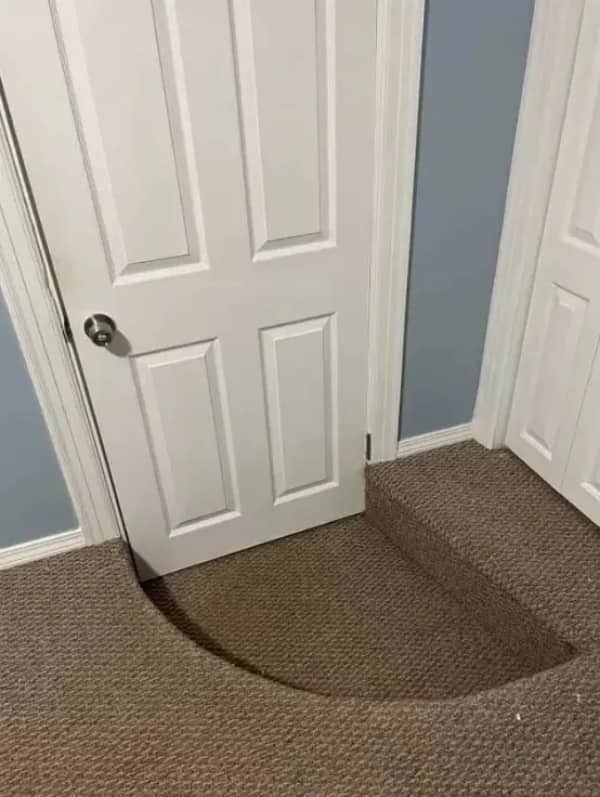 A white door positioned directly over a curved carpeted step, creating a major tripping hazard.