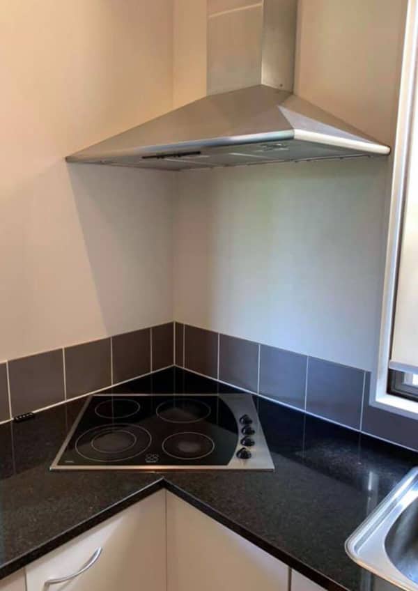 A glass stovetop installed directly into a corner, rendering half the burners unusable against the wall.