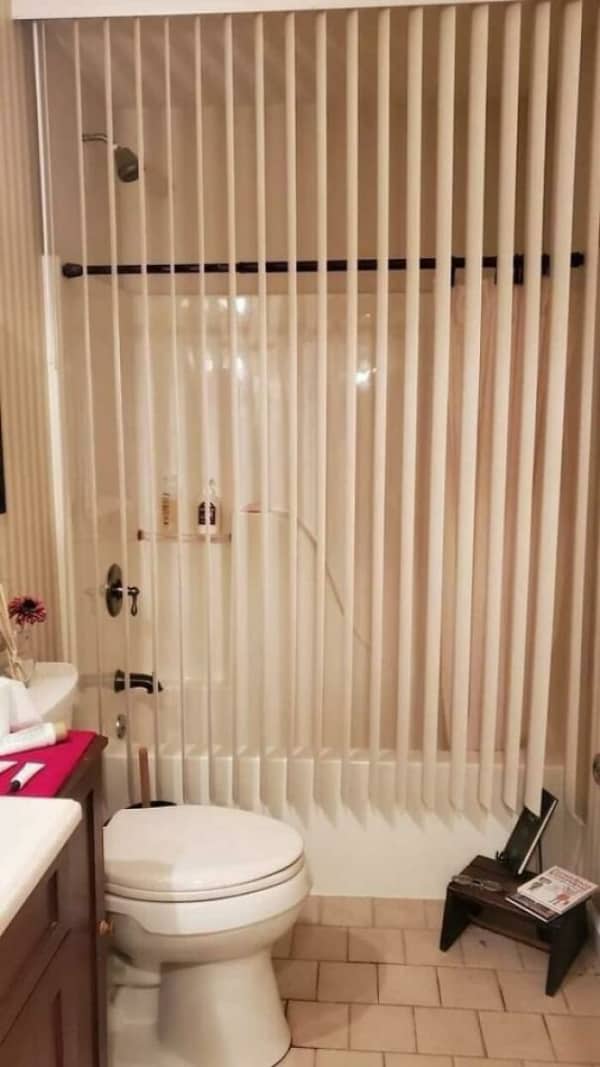 Vertical office-style blinds used as a makeshift and highly impractical shower curtain for a bathtub.