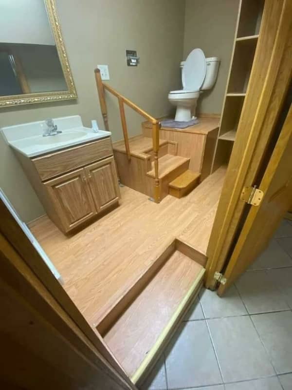 A toilet perched atop a steep flight of wooden stairs inside a cramped, carpeted bathroom.