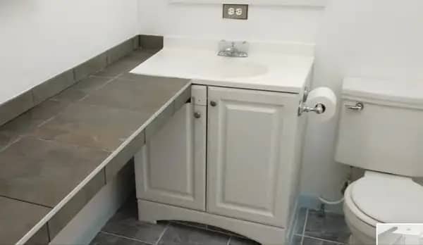 A bathroom vanity with a countertop that extends past the cabinet and blocks the toilet.