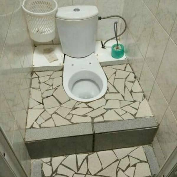 A toilet installed on a platform covered in a chaotic mosaic of broken white tiles.