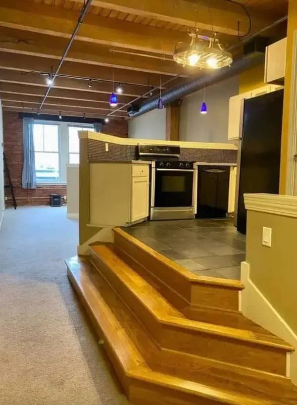 An open-concept kitchen built on a high wooden platform with steep, dangerous steps into the living room.