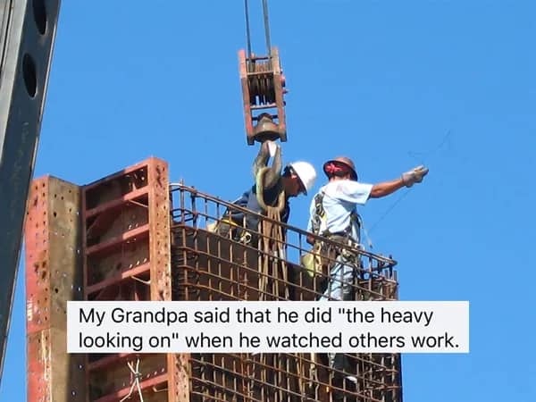 Two construction workers high up on scaffolding with a crane in the blue sky and a heavy looking on joke.