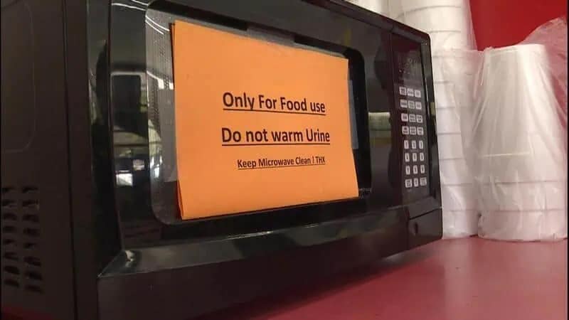 cursed image from a meme dump featuring a black microwave with a bright orange sign taped to the door that reads, "Only For Food use. Do not warm Urine," leaving viewers to wonder about the specific catastrophe that forced this warning into existence.