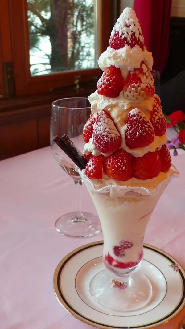 An impossibly tall strawberry sundae tower overflowing with fresh fruit, whipped cream, and chocolate sticks, standing as a monument to over-the-top dessert indulgence.