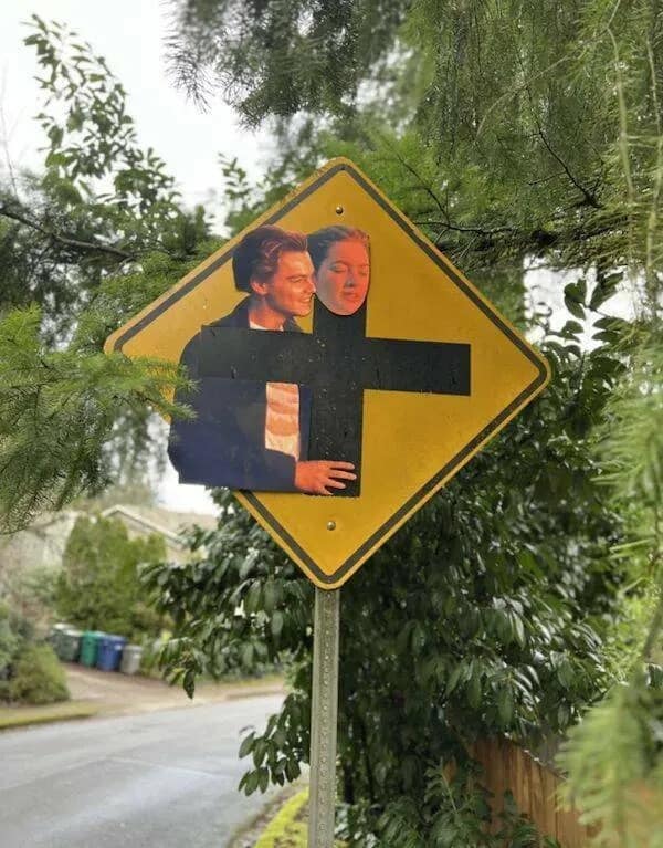 street art funny meme where someone perfectly aligned cutouts of Leonardo DiCaprio and Kate Winslet from Titanic onto a yellow intersection road sign so it looks exactly like the iconic "I'm flying" scene.