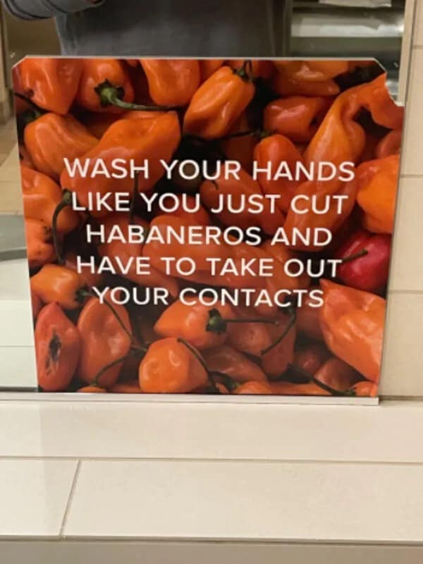 Bathroom sign over a background of spicy peppers commanding people to wash their hands as if they just cut habaneros and need to remove contact lenses. Highly effective funny memes.
