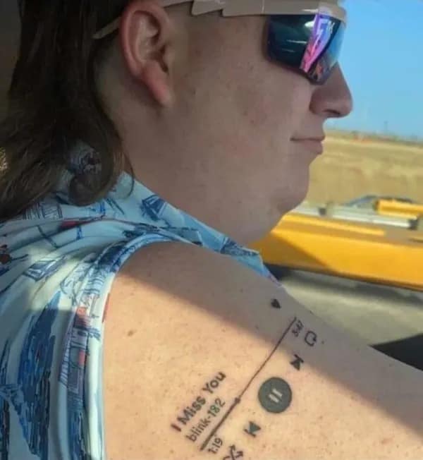internet meme showing a guy with a mullet and sunglasses proudly displaying an arm tattoo of a Spotify media player playing I Miss You by blink-182, radiating pure 2000s pop-punk energy in this meme dump.