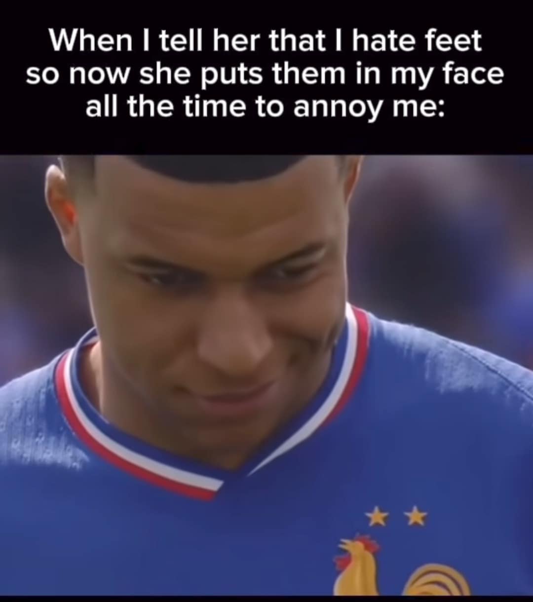 relatable relationship funny meme using a photo of Kylian Mbappé looking downward with a strained, slightly forced smile, perfectly capturing the exact reaction to a partner deliberately putting their feet in your face just to annoy you.