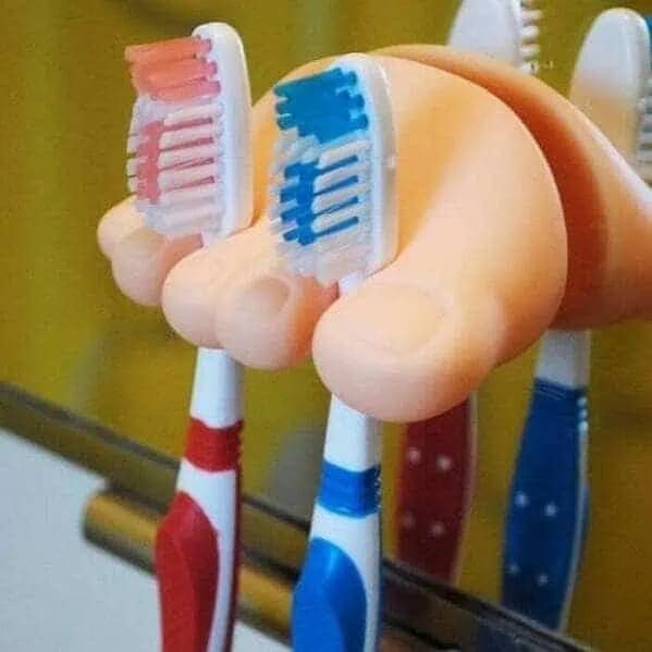 A "cursed" image of a bathroom vanity featuring a toothbrush holder shaped like a giant, fleshy human foot with toothbrushes wedged between the large plastic toes.