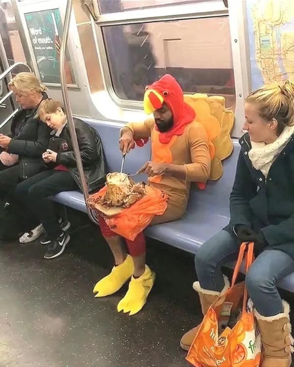 A chaotic and funny meme captured on a subway train where a man dressed in a full turkey costume is casually carving a roasted turkey on his lap while other passengers look on.