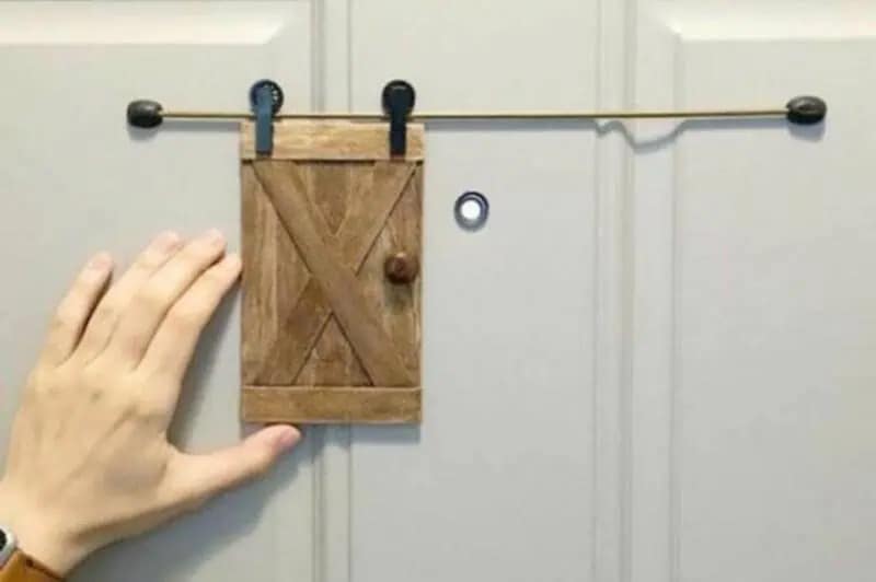 relatable funny meme for fans of the "farmhouse" aesthetic showing a miniature, fully functional sliding barn door used as a cover for a standard apartment door peephole