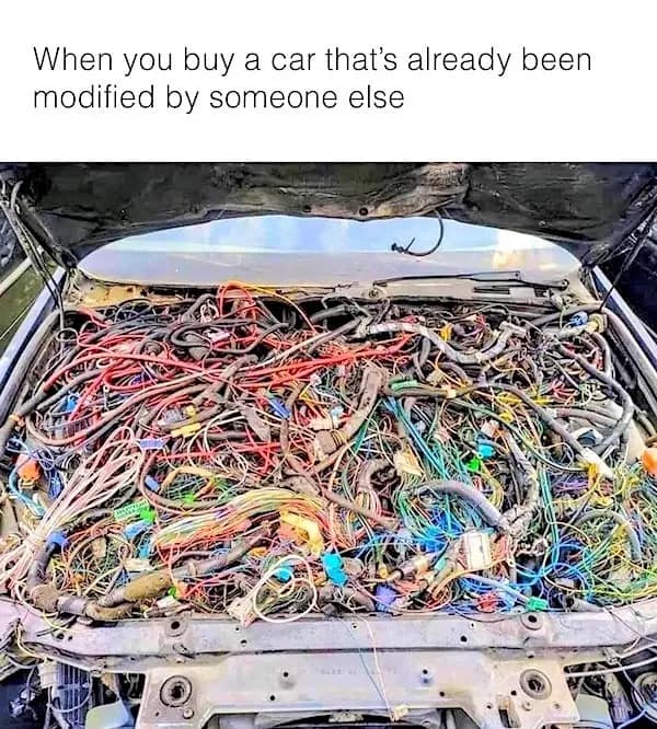 mechanic’s worst nightmare featured in a meme dump showing a car with its hood popped. Instead of a tidy engine, the bay is an absolute bird's nest of hundreds of tangled, multi-colored wires, captioned: "When you buy a car that’s already been modified by someone else."