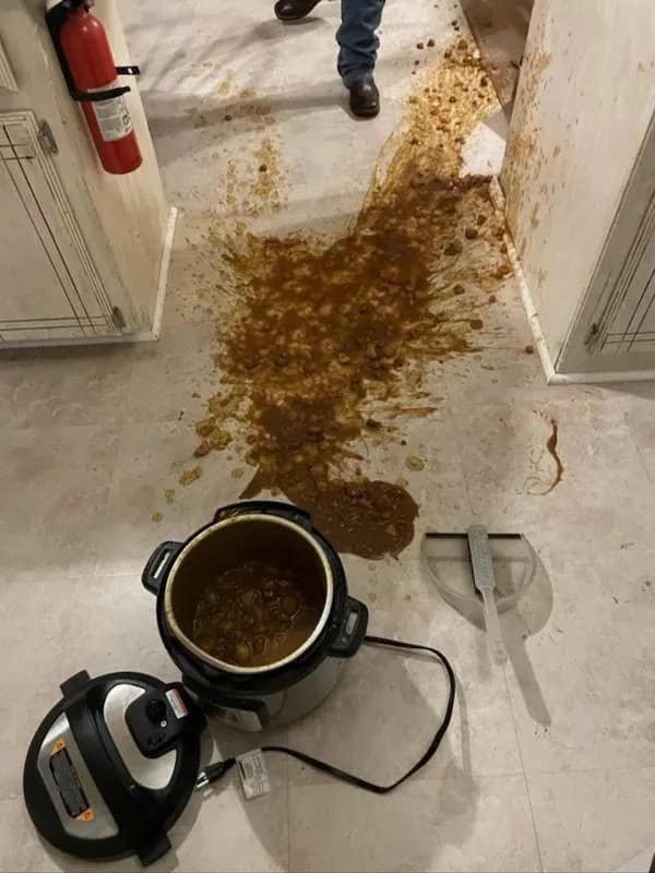 This hilarious meme features a visceral kitchen nightmare: a massive crockpot spill of brown stew that has exploded across a white tile floor and splattered the surrounding cabinetry.