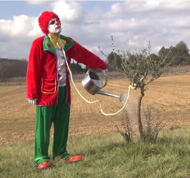 A completely cursed and dark funny meme showing a depressed clown watering a barren tree while the watering can hose forms a noose around his neck, capturing pure internet exhaustion in this chaotic meme dump.