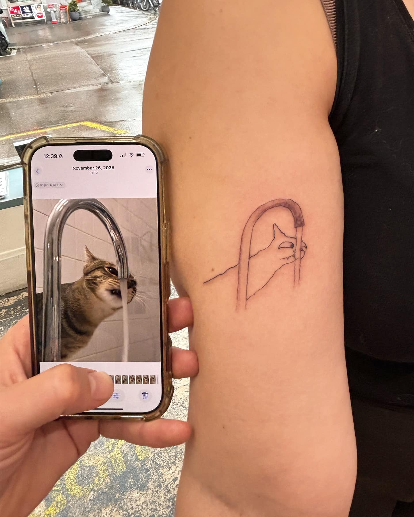 A brilliant funny meme showing a person comparing an incredibly terrible line-art tattoo on their arm to the actual photo of a derpy cat drinking from a faucet, proving the artist matched the weirdness perfectly in this meme dump.