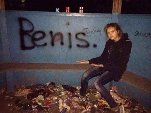 gritty hilarious meme from a meme dump featuring a woman posing proudly in an abandoned, trash-filled shelter in front of a blue wall with the word "Benis." spray-painted in large black letters, capturing peak low-budget internet humor.