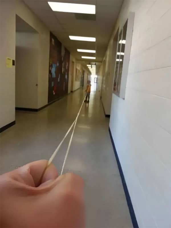 A POV shot of a hand stretching a long rubber band aimed at a student.