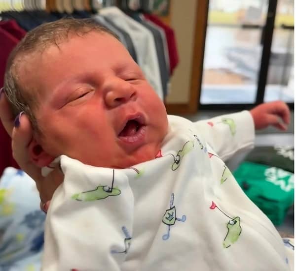 Newborn baby in golf pajamas looking like a tiny man exhausted after a long workday.