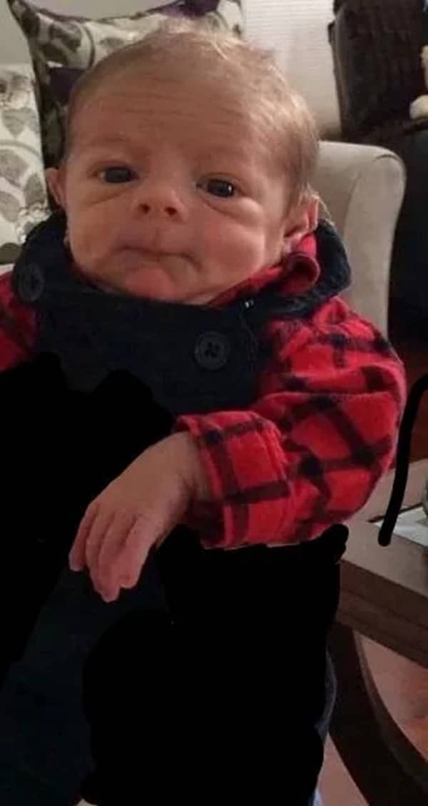 Baby in a red flannel shirt with deep forehead wrinkles looking like a seasoned lumberjack.