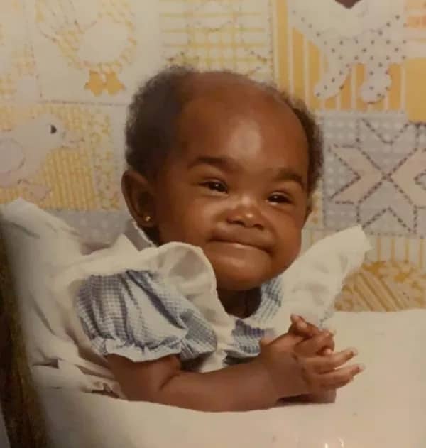 Smiling baby with a high hairline and folded hands looking like they are leading a board meeting.